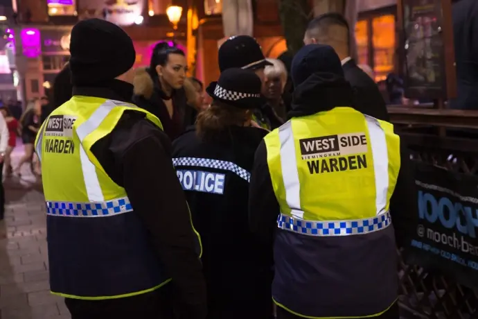 Two Westside Birmingham street wardens in hi-vis and a police officer on a busy Birmingham nightlife street at night
